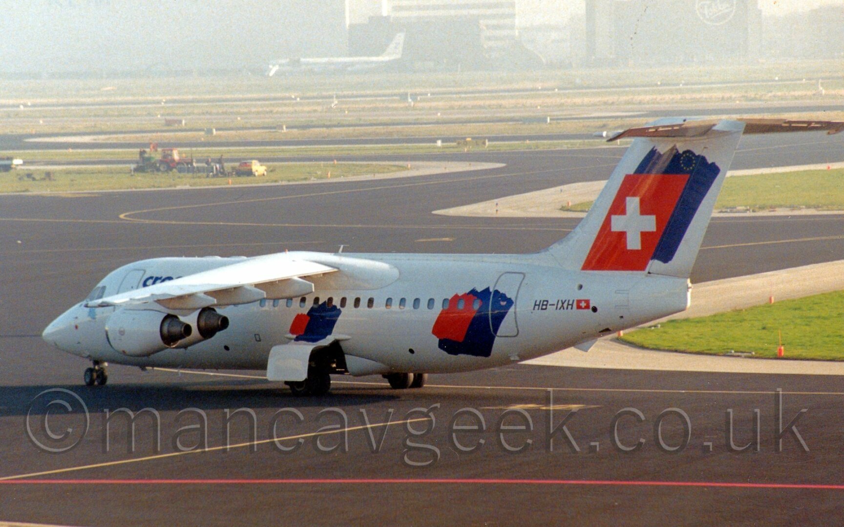 Small white 4 engined jet airliner with red and blue splotches denoting the Swiss and EU flags, respectively.