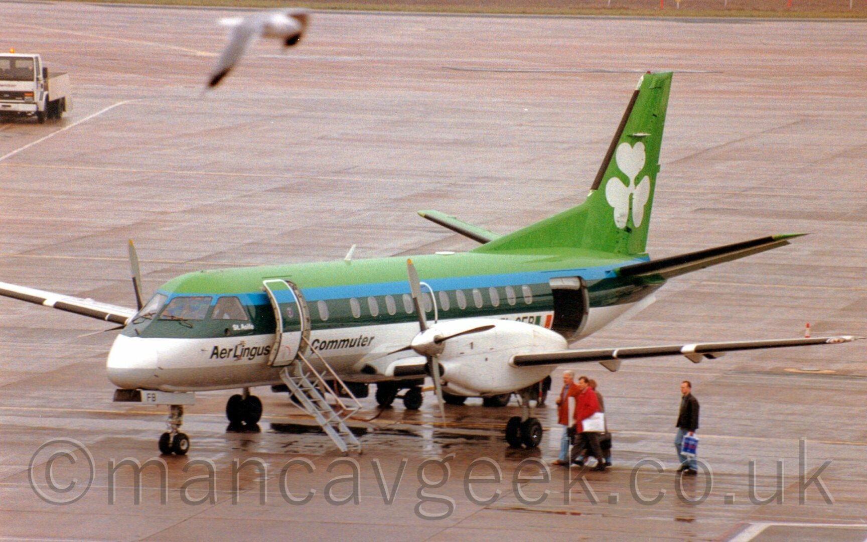 Green and white propellor airlines with a white shamrock on the tail.
Some passengers are walking across the tarmac to board the plane.
