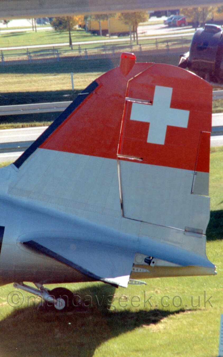 Closeup on the tail of a World War 2 era propellor airliner.
The tail is silver, with a red stripe depicting the Swiss flag.