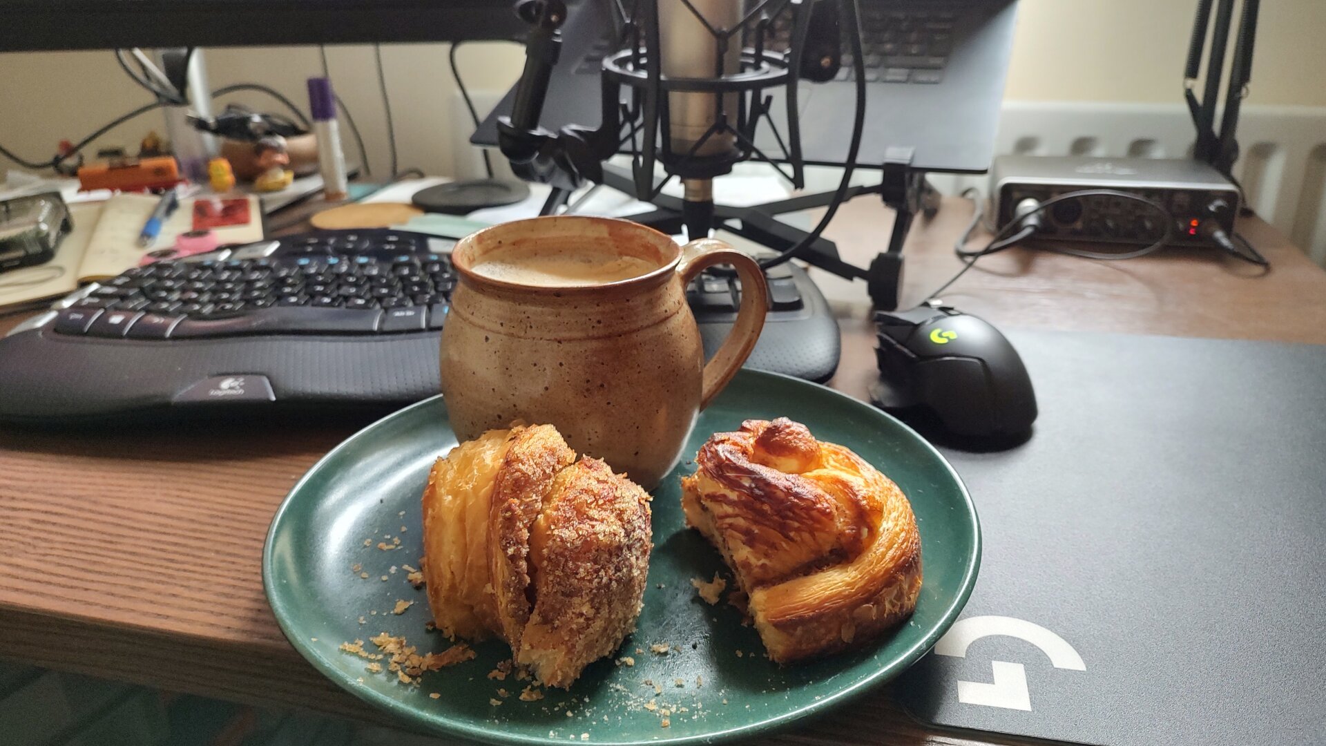 desktop with keyboard and mouse in the background, foreground showing a large plate with big coffee mug and two pieces of delicious pastry