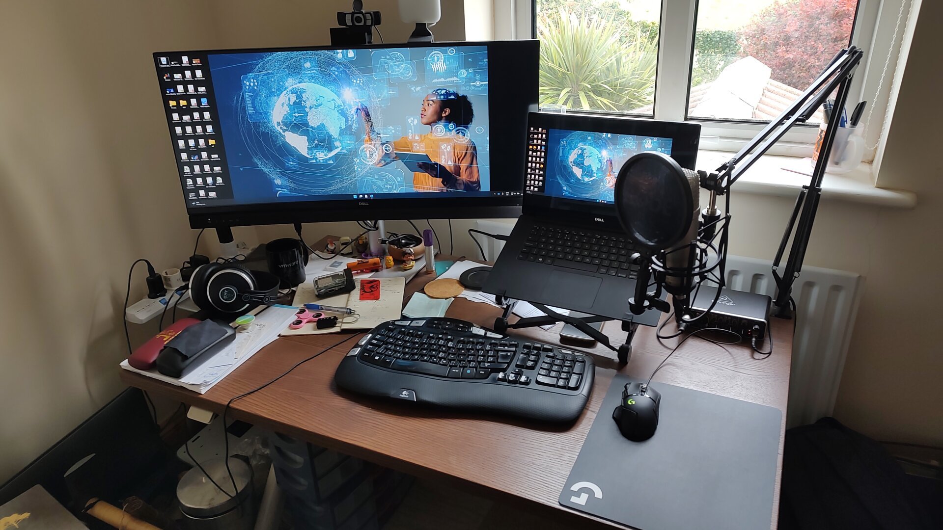 desktop with two monitors, laptop, keyboard, mouse, microphone, headphones, and some other things