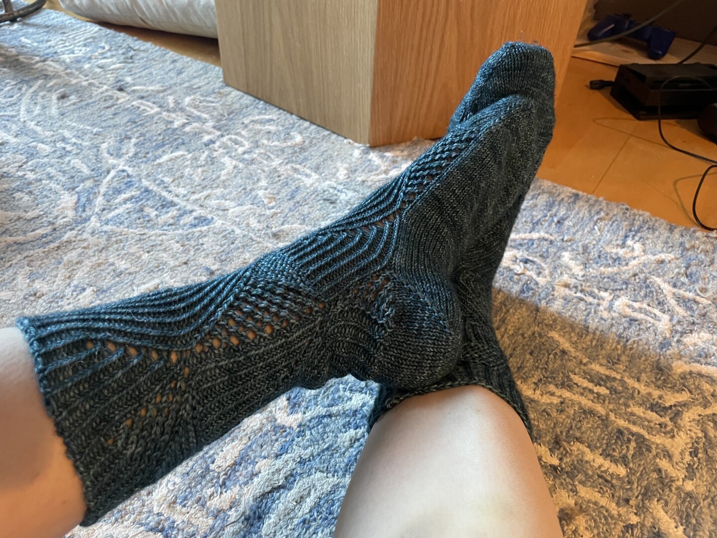 A picture of the side and insole of a knitted sock, on a foot. It has vertical waves made by a 1x1 rib and simple lace.