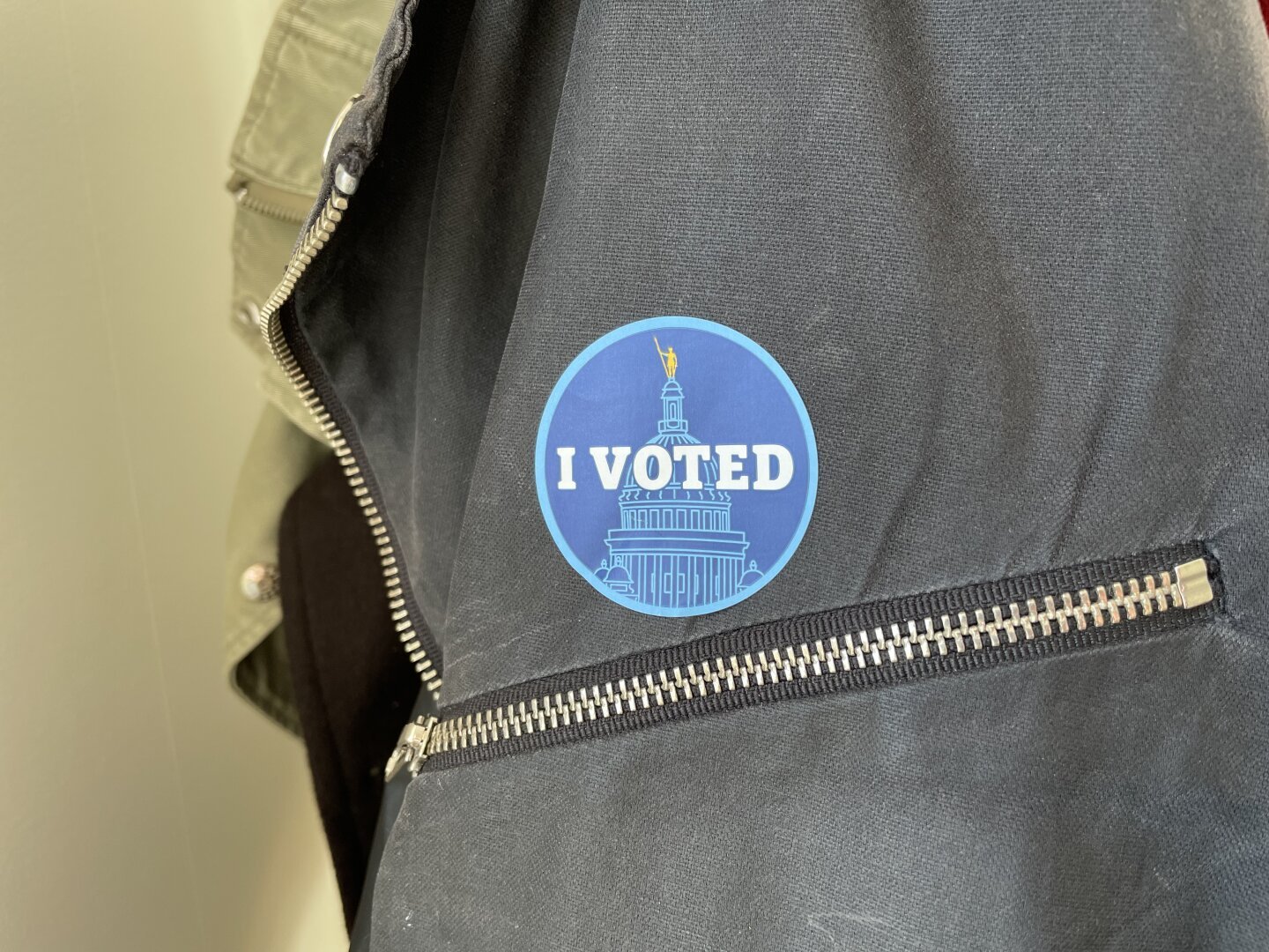 A round sticker that says “I voted”, stuck on a coat above a zipper”
